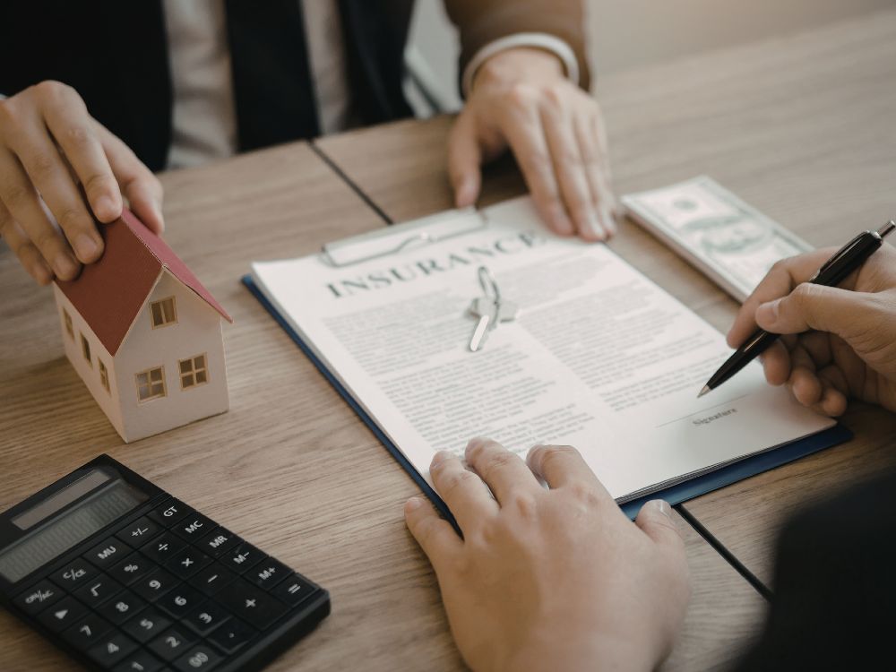 Assinatura de contrato com maquete de casa e calculadora sobre a mesa, simbolizando a formalização do Seguro fiança Curitiba no processo de locação.