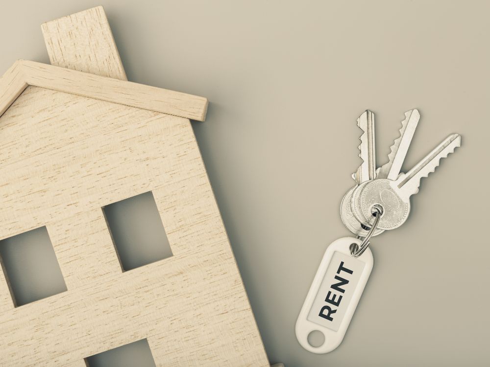 Chaves com etiqueta “rent” ao lado de casa de madeira simbolizam retorno financeiro ao investir em aluguéis e gerar renda passiva com segurança.