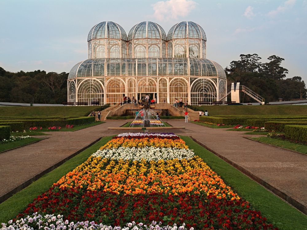 Jardim Botânico de Curitiba com canteiros floridos e visitantes, destacando áreas verdes e lazer ao ar livre como pilares da qualidade de vida em Curitiba.