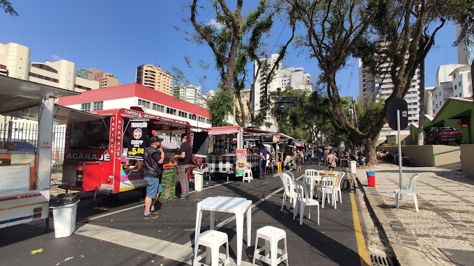 Food trucks organizados em rua arborizada na Feira do Batel, com opções gastronômicas variadas em Curitiba. O que é feira do Batel?