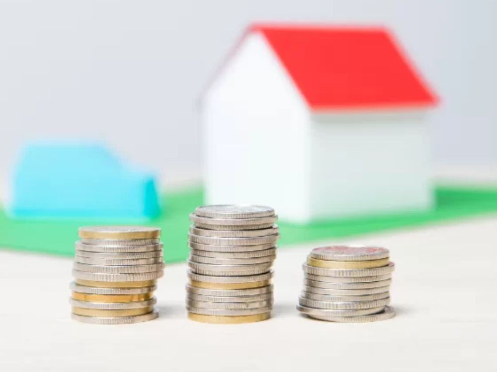 Casa em miniatura com pilhas de moedas representando custo de vida e investimentos imobiliários em Curitiba.