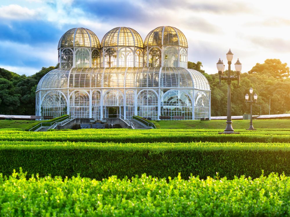 Jardim Botânico de Curitiba ao entardecer: Estufa icônica cercada por jardins verdes, um dos principais pontos turísticos de Curitiba.