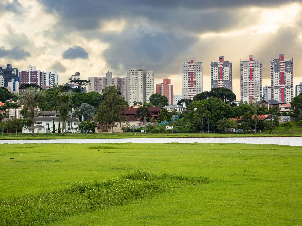 Lago cercado por área verde e edifícios residenciais em Curitiba, destacando qualidade de vida.