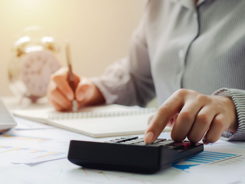 Pessoa escrevendo com calculadora e documentos na mesa. Organização financeira e planejamento para regularização em como pagar IPTU atrasado Curitiba.