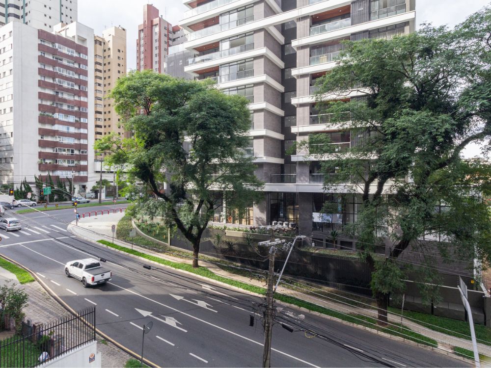 Rua arborizada e edifício moderno no Bairro Água Verde Curitiba, mostrando a mistura de urbanização e áreas verdes que tornam o bairro bom para morar.