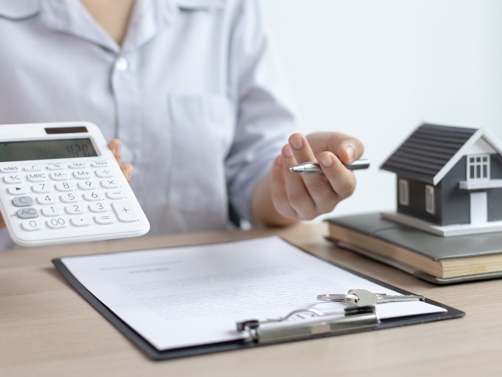 Calculadora branca e maquete de casa em cima de documentos. Simulação de valores e negociação de dívida ativa em como pagar IPTU atrasado Curitiba.