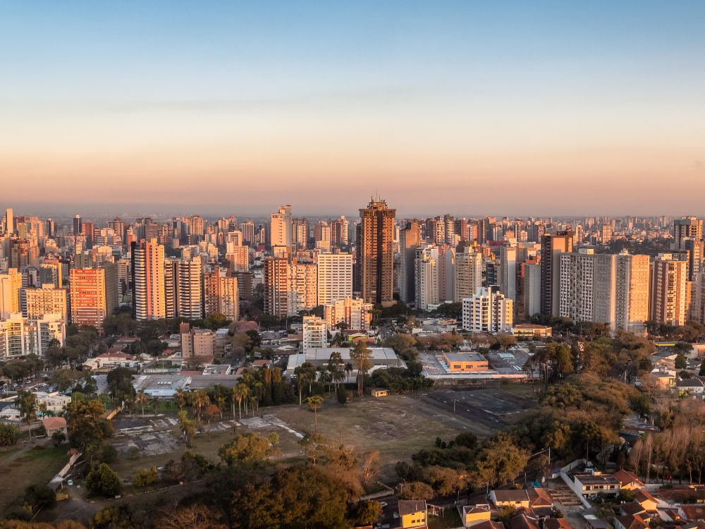 Panorama de Curitiba ao entardecer, com prédios iluminados pelo pôr do sol, representando a modernidade e qualidade de vida da cidade. Entenda se morar em Curitiba é caro ou barato
