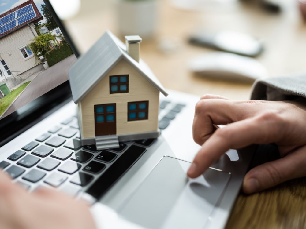 Pessoa navegando em site de imóveis com maquete de casa sobre notebook, simbolizando o uso da tecnologia para investir em Curitiba com segurança.