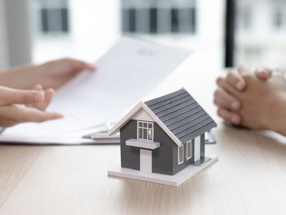 Duas pessoas discutem contrato com maquete de casa na mesa, ilustrando negociação para investir em Curitiba em imóveis residenciais.