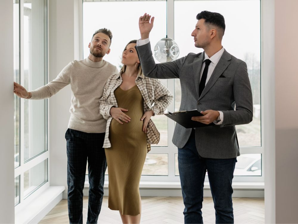 Casal jovem em visita guiada por corretor durante tour em imóvel, avaliando opções de compra para investimento no mercado imobiliário.
