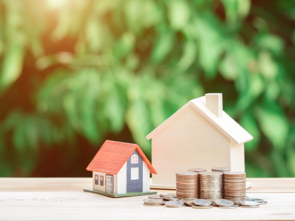 Casas em miniatura com moedas empilhadas ao lado, simbolizando planejamento financeiro e valorização no investimento no mercado imobiliário.