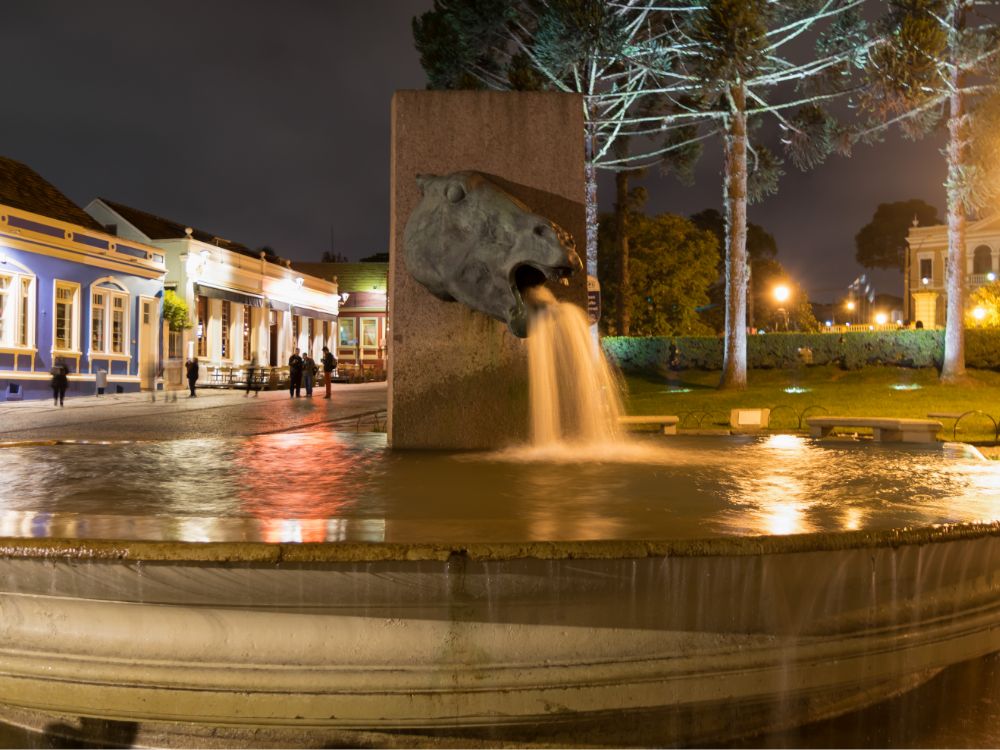 Fonte da Praça Tiradentes, iluminada à noite, com a arquitetura histórica ao fundo, uma excelente opção para passeios em família.