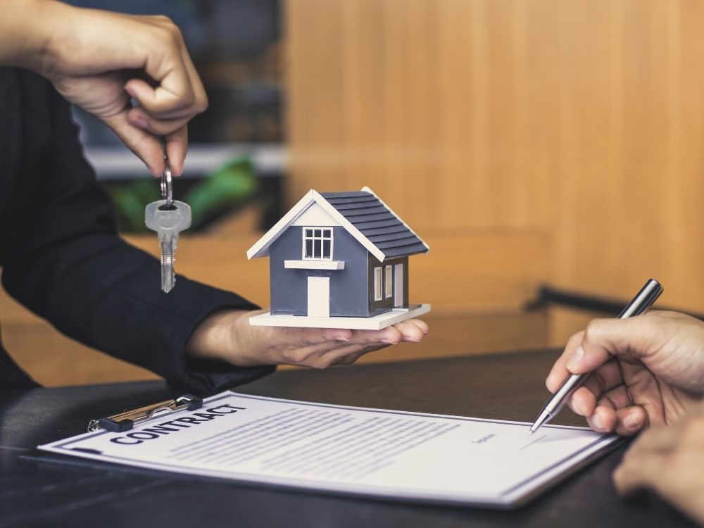 Contrato de locação sendo assinado enquanto uma pessoa segura uma miniatura de casa e uma chave, representando como alugar um apartamento sem fiador.