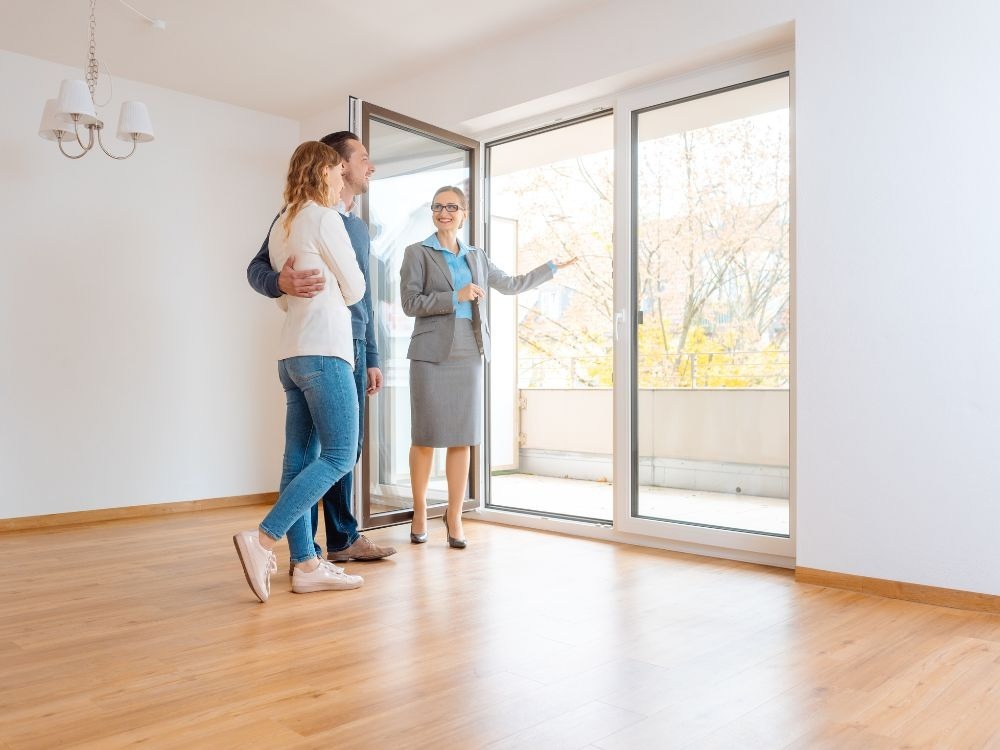 Casal acompanhando corretora em visita a um imóvel iluminado e amplo, simbolizando as possibilidades de como alugar um apartamento sem fiador.