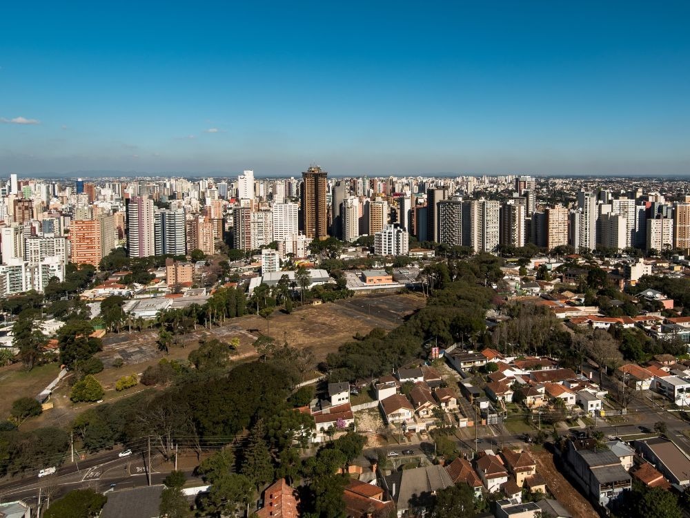 Foto diurna do Jardim Botânico de Curitiba, com sua estufa de vidro icônica. O cartão postal sugere a qualidade de vida, ideal para as Melhores cidades para investir em imóveis.