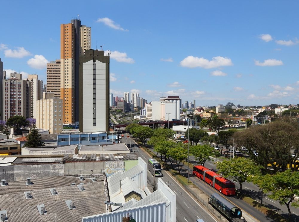 : Imagem de um bairro com edifícios altos e modernos em Curitiba, com ruas limpas e bem arborizadas. A foto ressalta o potencial imobiliário da cidade, uma das Melhores cidades para investir em imóveis.