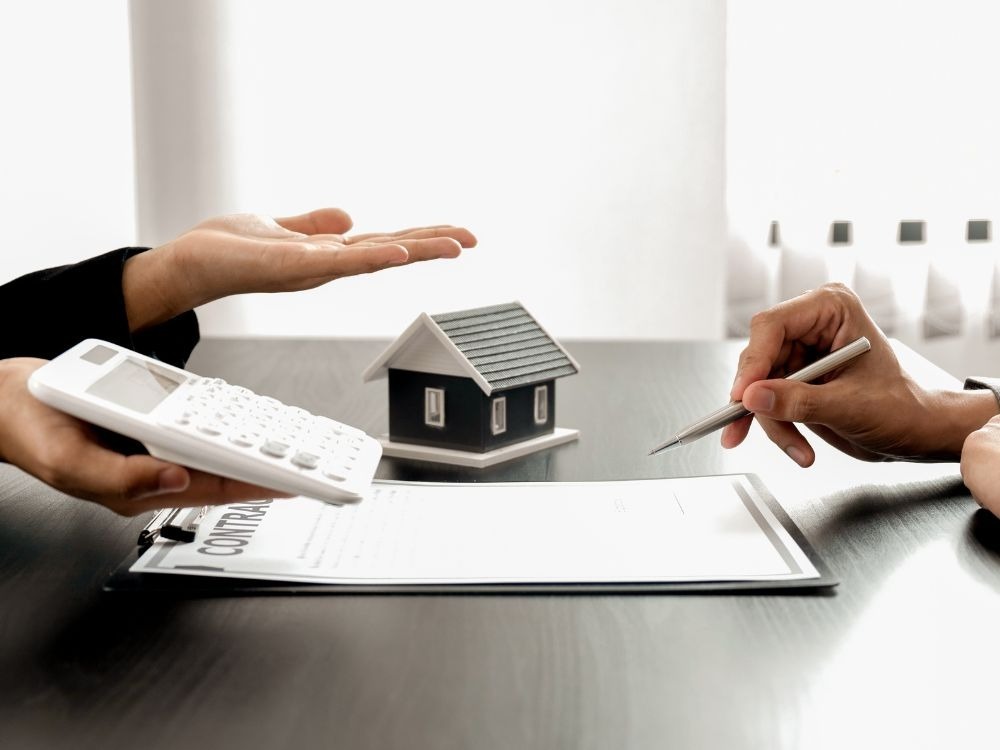 Negociação de contrato com uso de calculadora e maquete de casa — veja quanto cobrar de aluguel considerando despesas e valorização do imóvel.