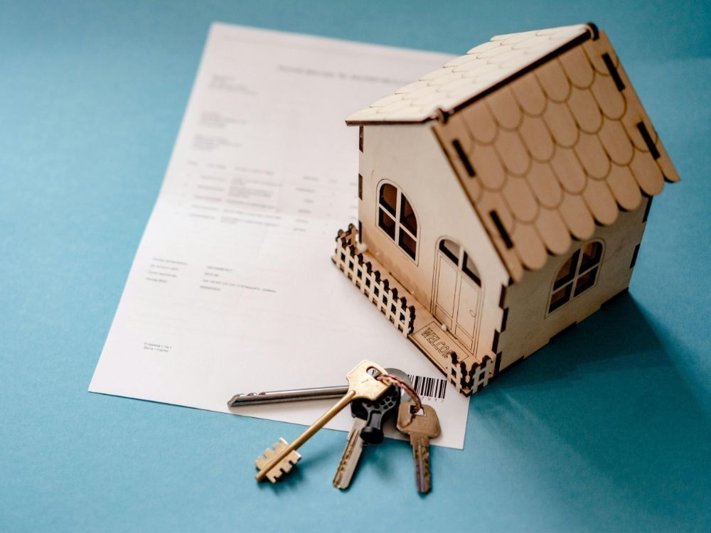 Contrato de locação com chaves e miniatura de casa representando o processo de como alugar um apartamento sem fiador.