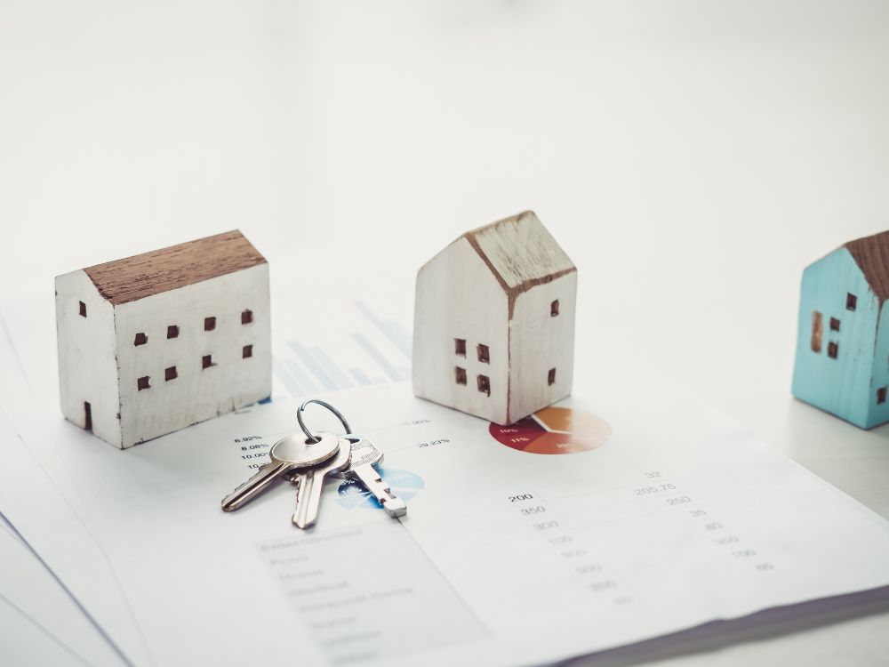 Miniaturas de imóveis com chaves sobre relatório financeiro ilustrando como funciona o título de capitalização para aluguel