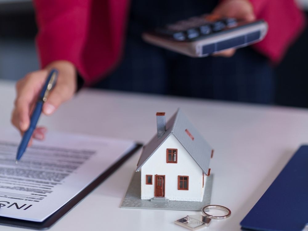 Contrato de locação sendo analisado com calculadora e modelo de casa, reforçando as vantagens de alugar com imobiliária no suporte financeiro e jurídico.