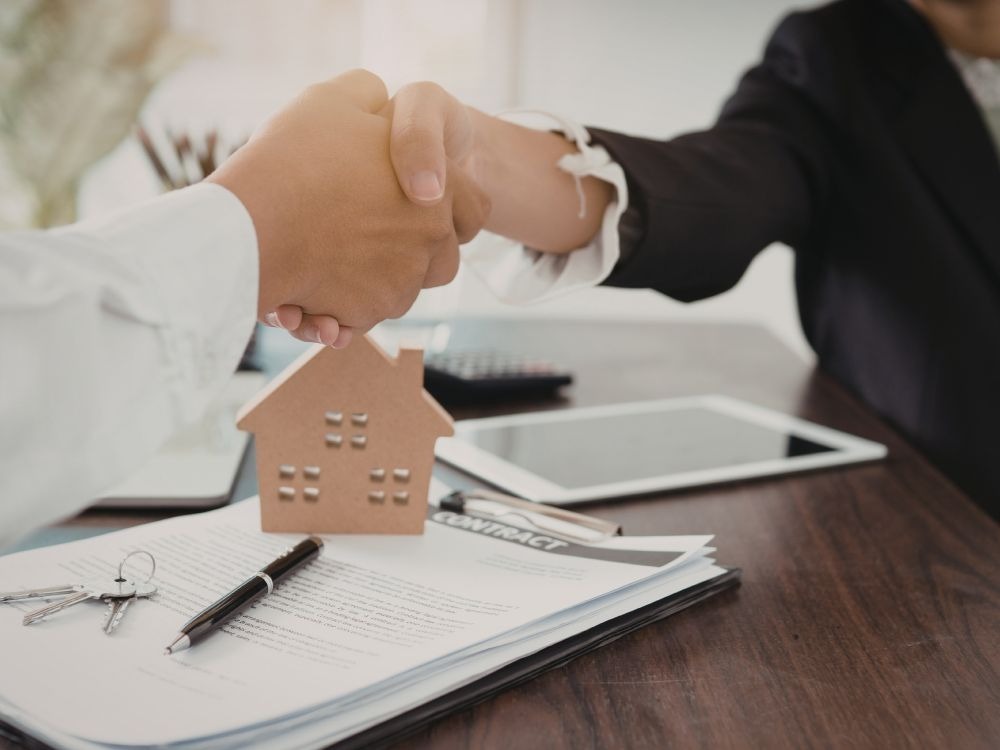 Aperto de mãos sobre contrato de aluguel com chave e miniatura de casa, representando as vantagens de alugar com imobiliária na formalização do acordo.