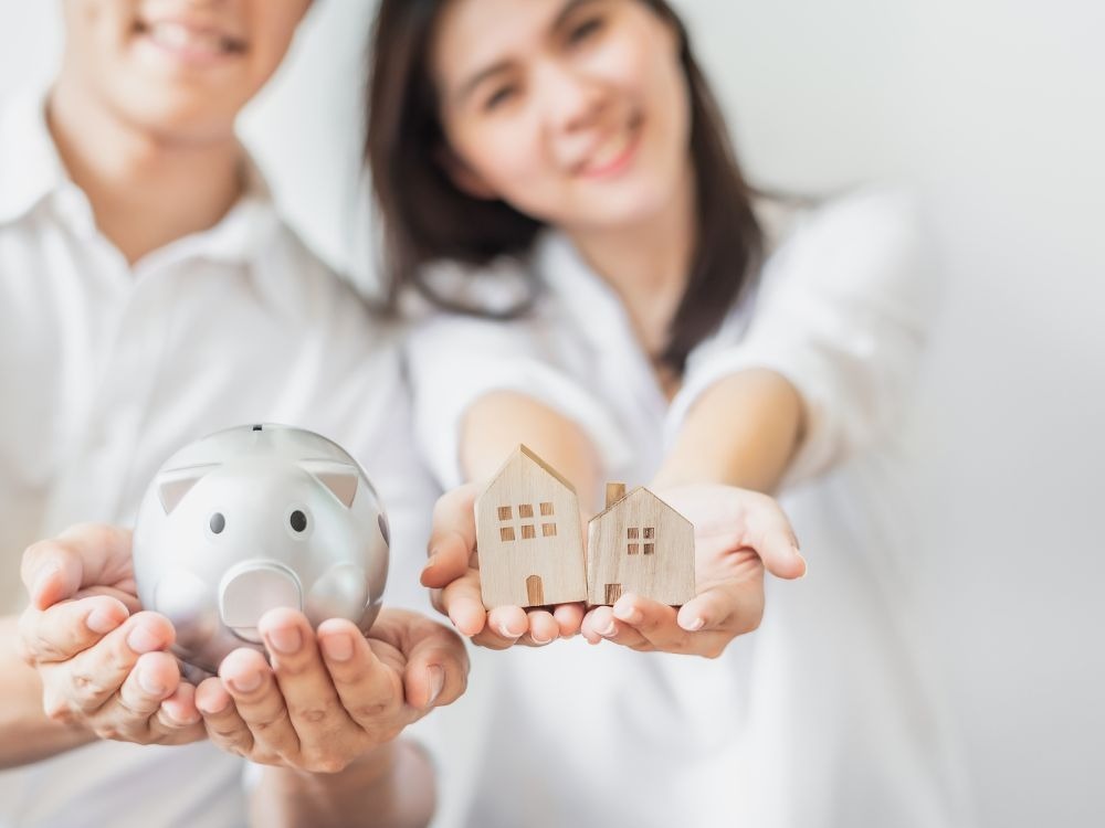 Casal segurando cofre e casas em miniatura, ilustrando o conceito de planejamento financeiro e o que é fundo de reserva em imóveis.