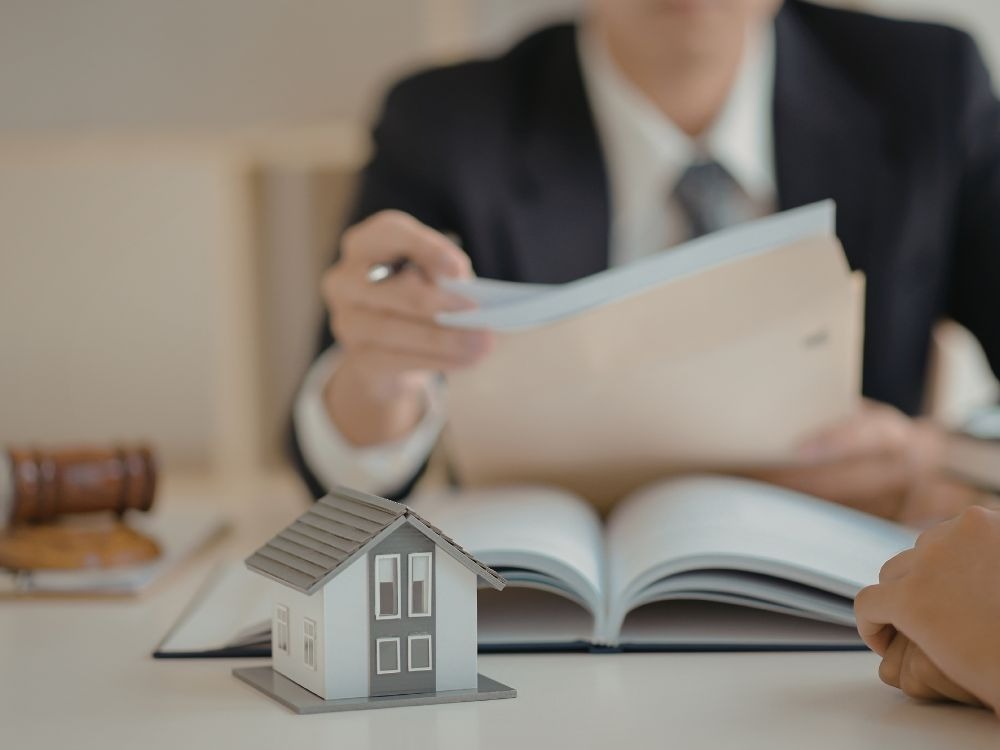 Profissional analisando documentos jurídicos com maquete de casa em destaque, reforçando a relevância do CPF dos imóveis para identificação e controle patrimonial.