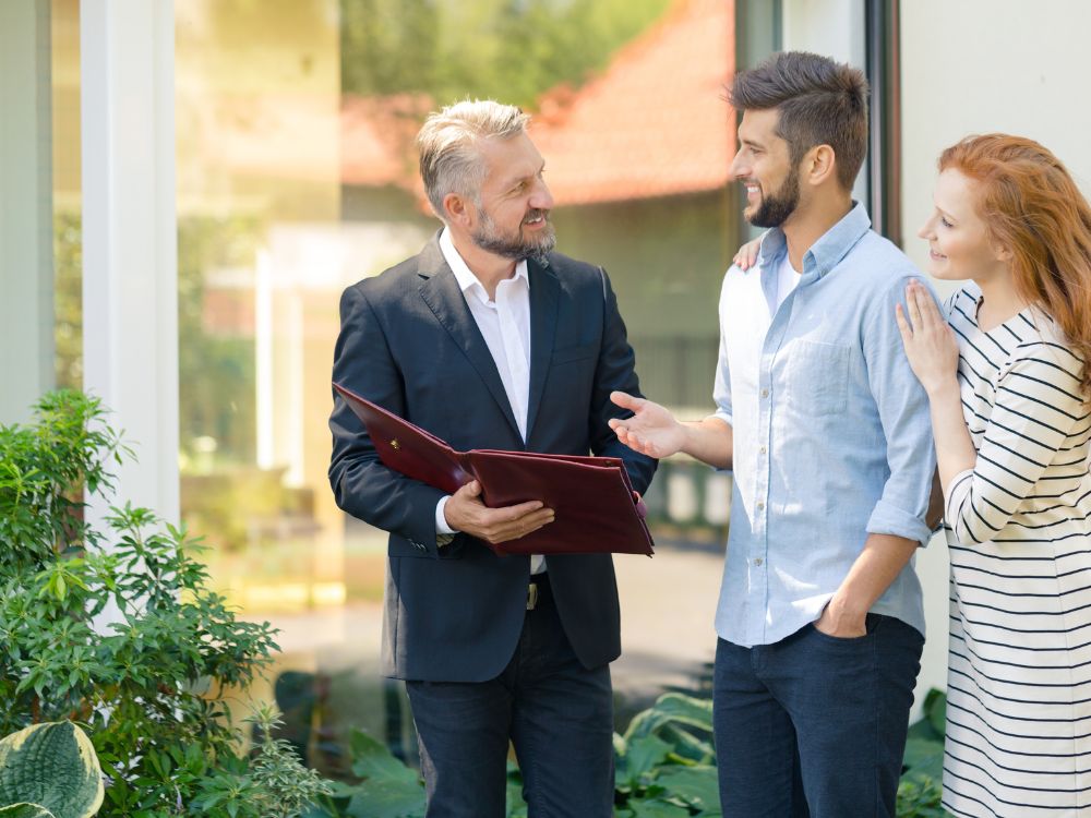 Atendimento imobiliário com corretor apresentando imóvel a casal interessado, contexto explicativo sobre o que faz a imobiliaria no processo de compra