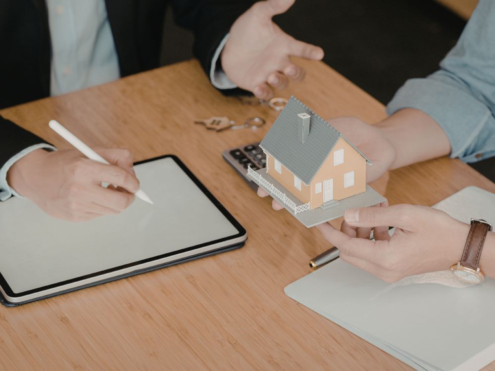 Negociação com maquete de casa e contrato avaliando se vender imóvel sem corretor é o ideal