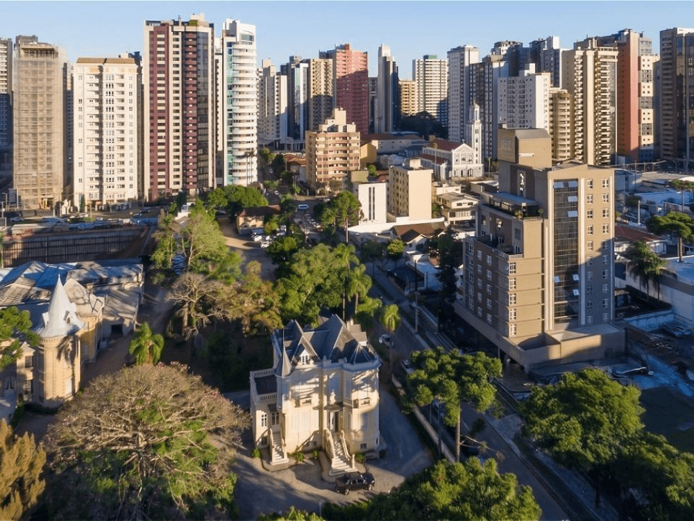 Vista aérea do bairro Batel com edifícios altos, áreas arborizadas e imóveis de alto padrão em Curitiba.