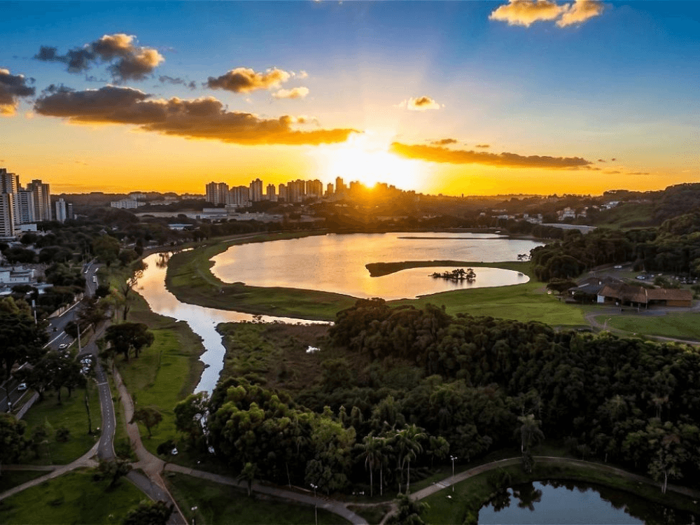 Paisagem com lago, áreas verdes e horizonte urbano ao entardecer representando a qualidade de vida no Bigorrilho em Curitiba.