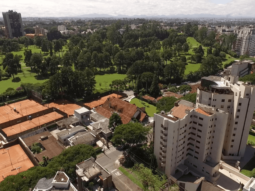Vista aérea do bairro Cabral com prédios residenciais, quadras esportivas e extensa área arborizada em Curitiba.